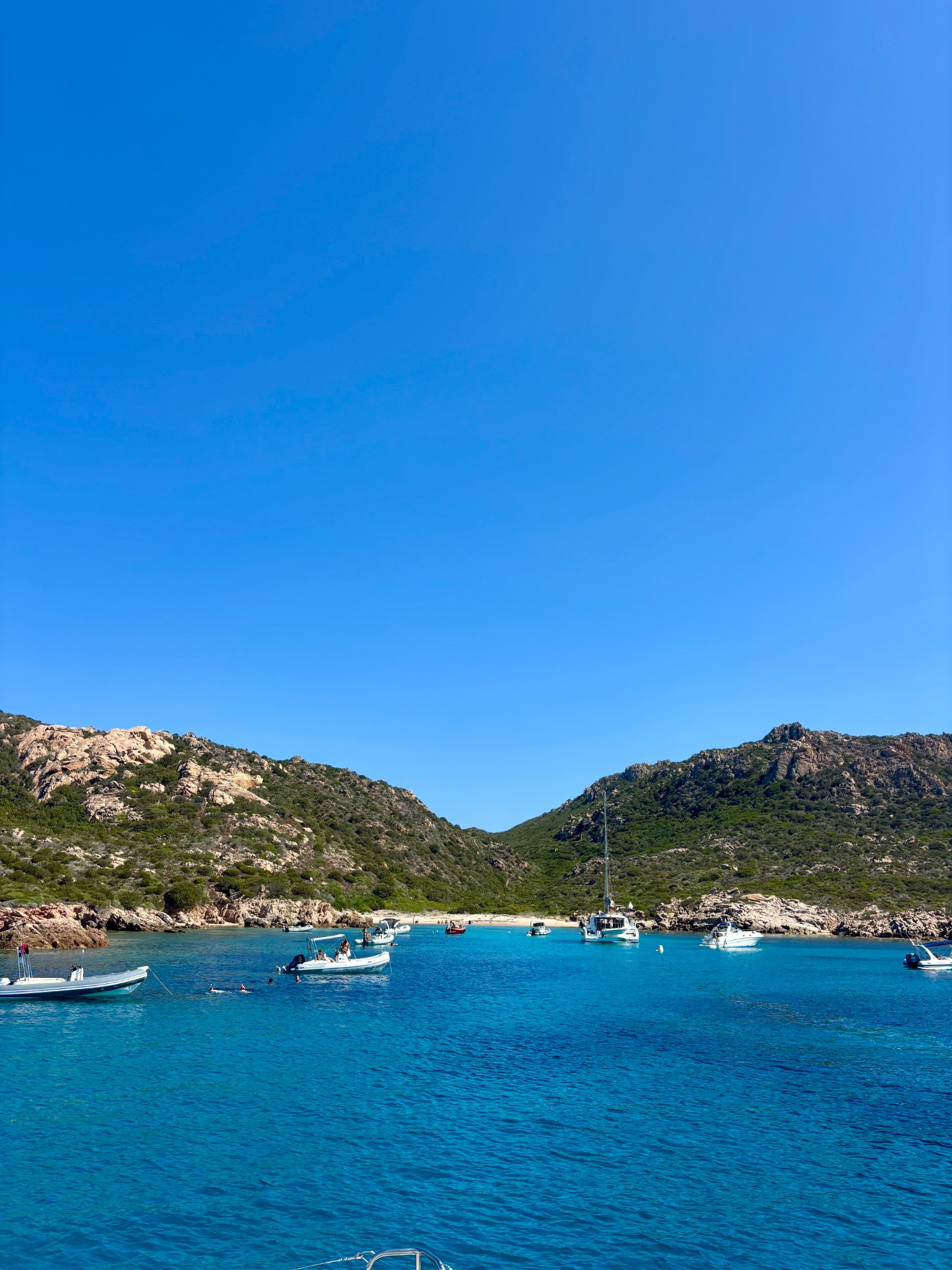 Small boats in a blue Sardinian cove framed by rocky hills